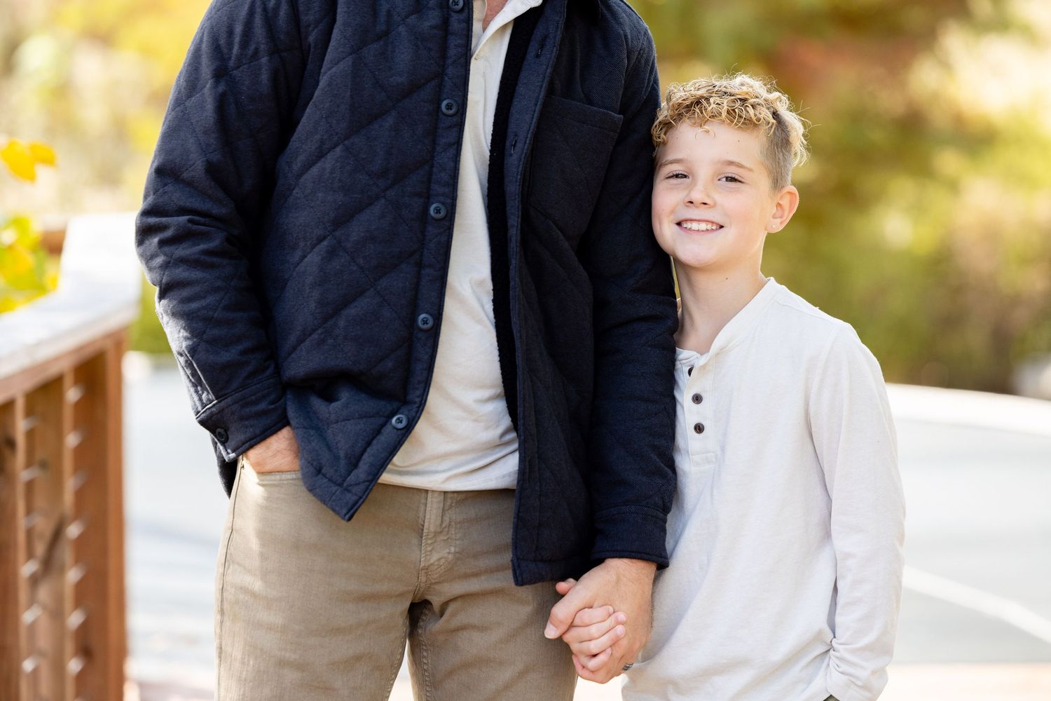 A young boy and his father standing together and smiling in a natural outdoor setting.