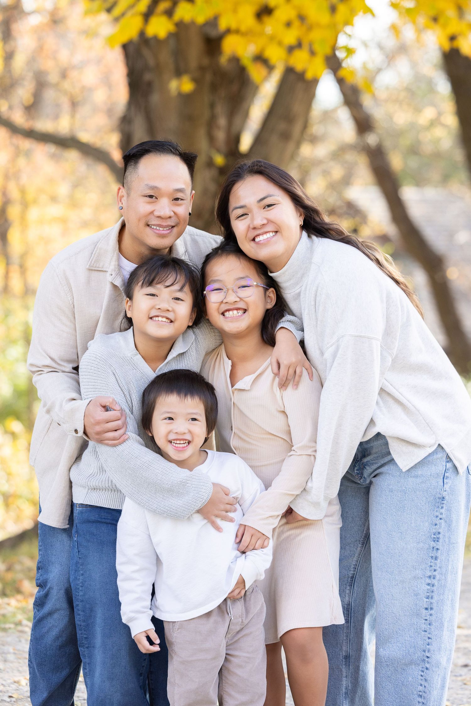 A happy family of five, including parents and three children, posing for a portrait in an outdoor setting.