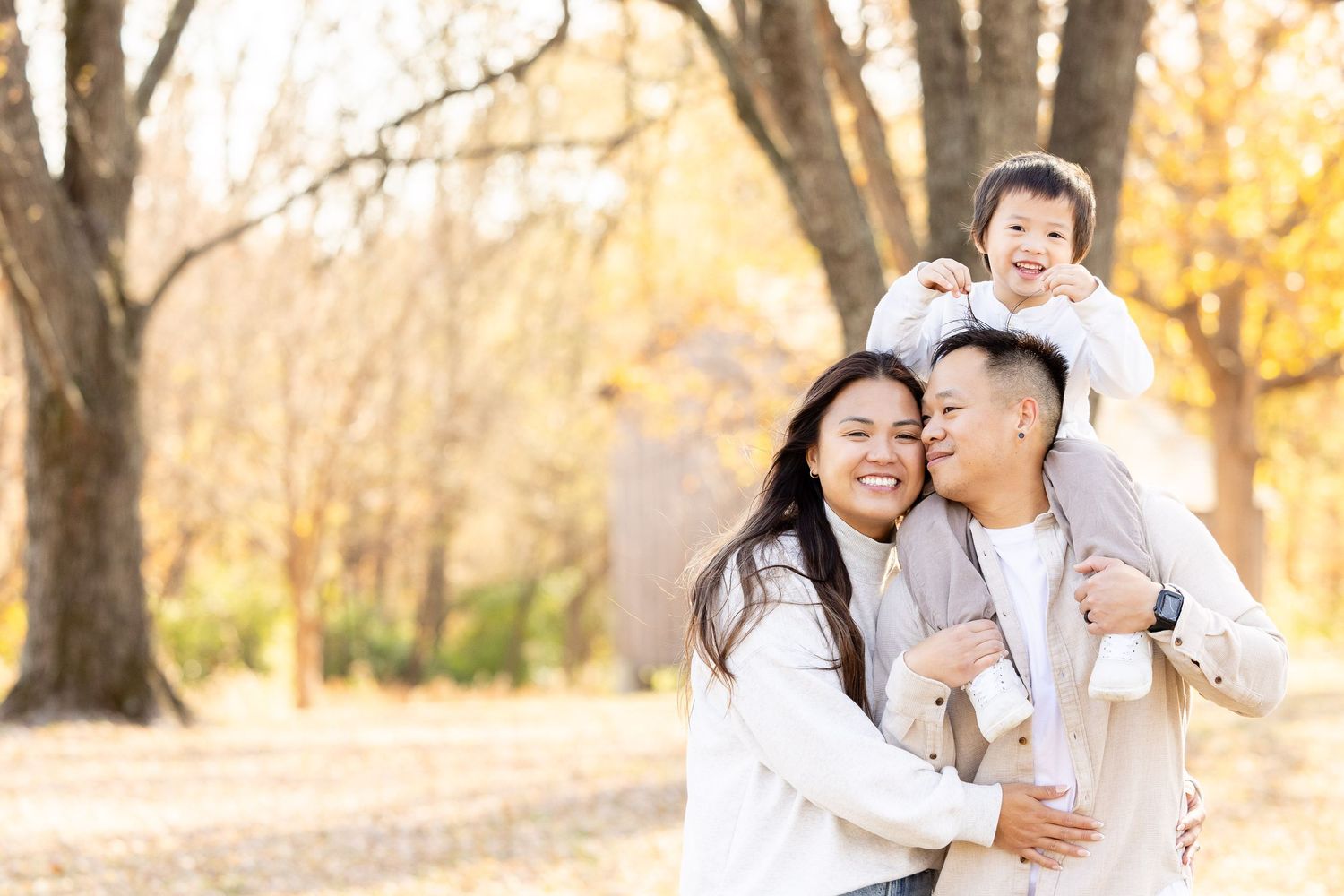 A family of four, including parents and two children, embracing and smiling in a park-like setting.