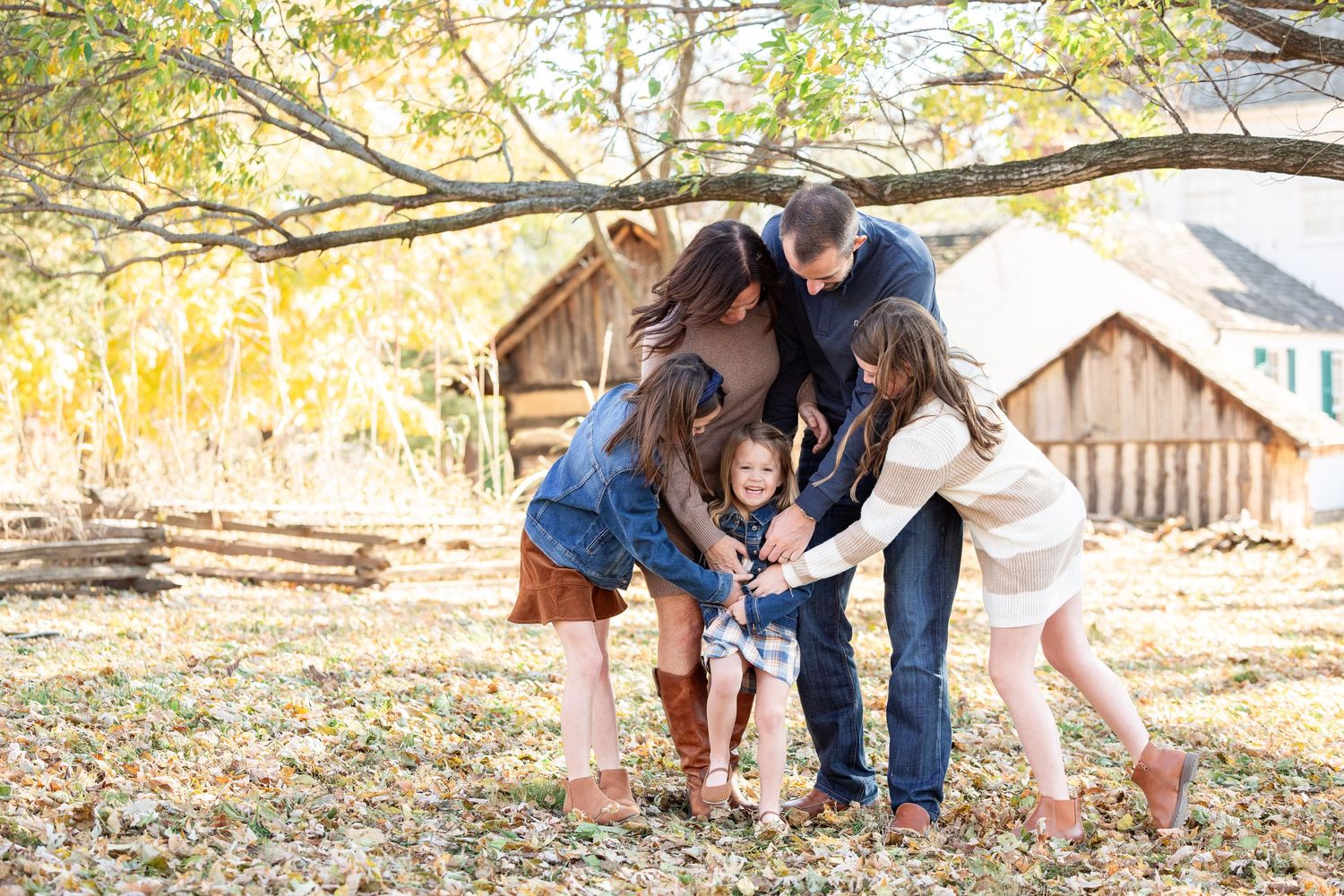 A family of four, including parents and two children, embracing and posing together in a rural outdoor setting.