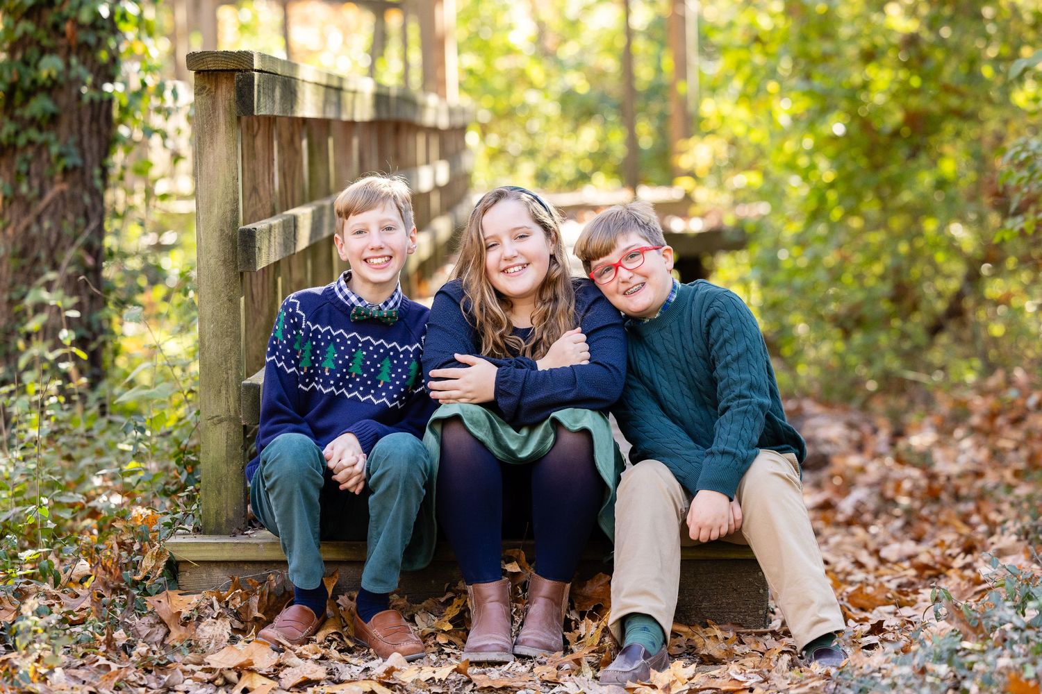 Three children sitting on a wooden bench in a forest setting.