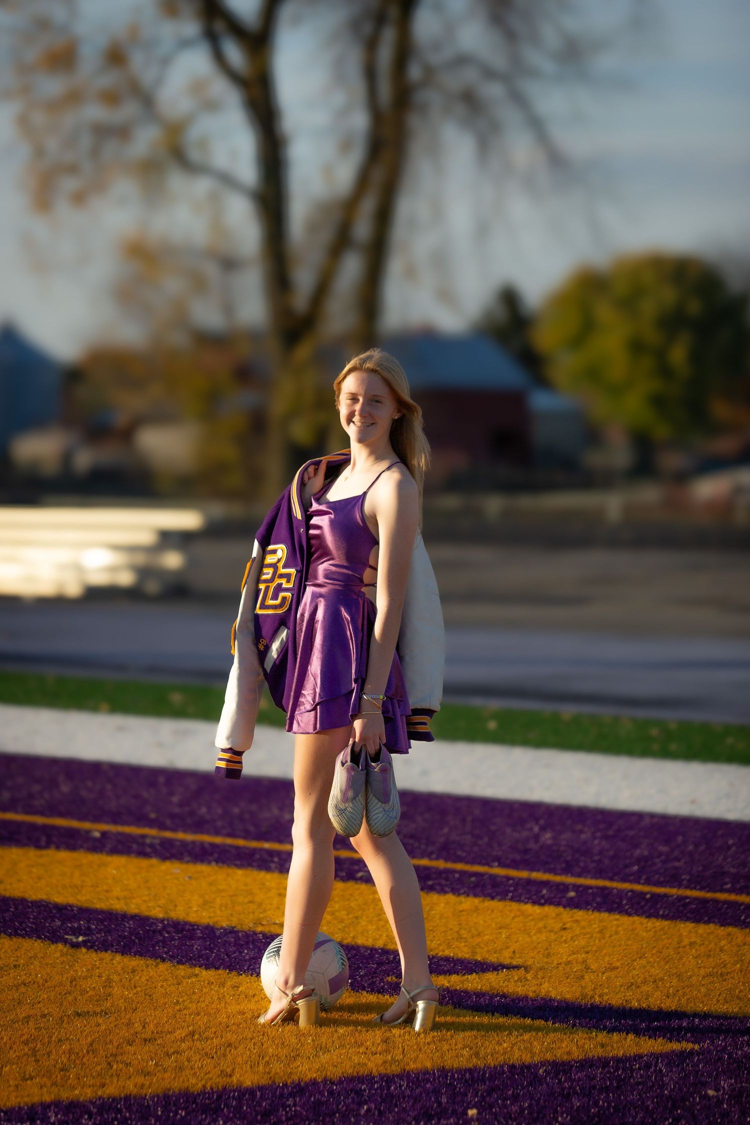 A cheerleader in a purple dress and heels poses on a colorful striped surface during golden hour lighting.