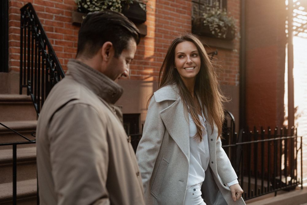 A couple in coordinating coats sharing a warm moment outside a brick building.