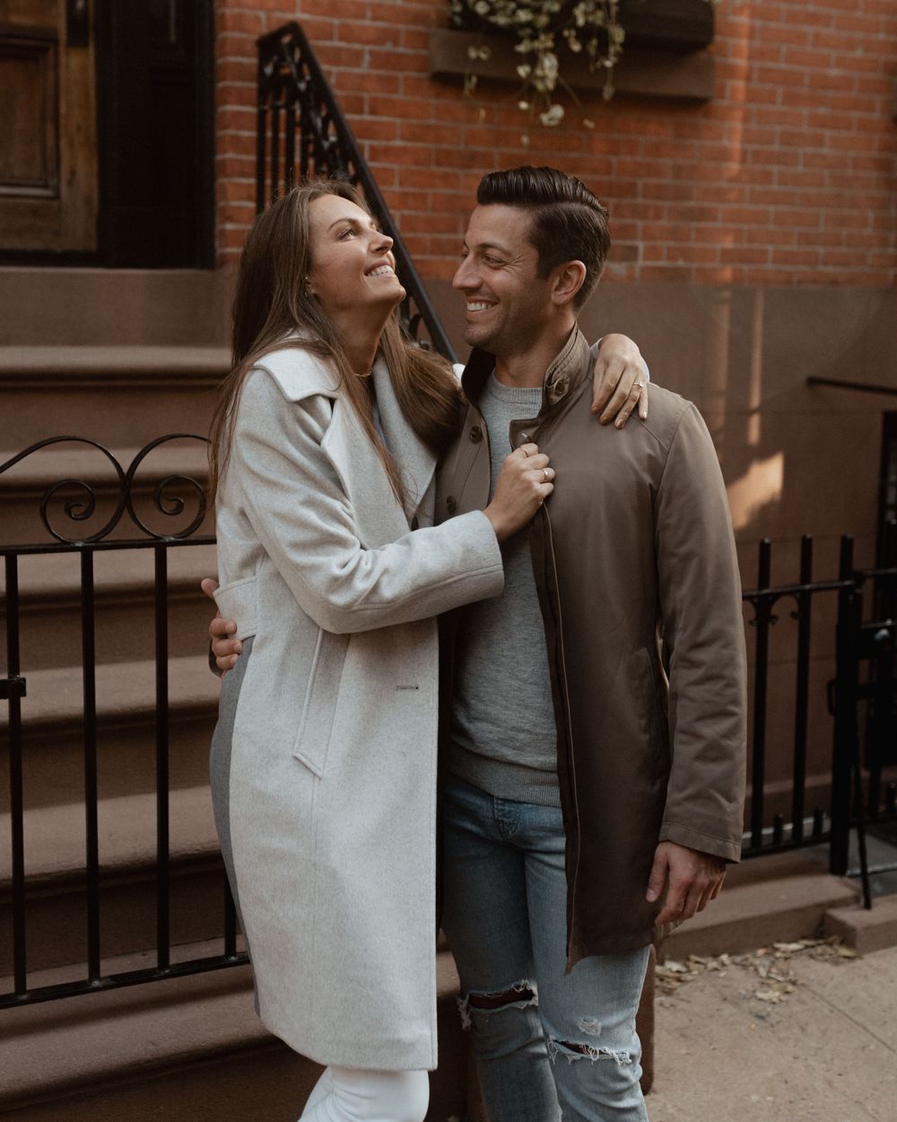 A couple in coordinating outfits sharing an affectionate moment against brick architecture.