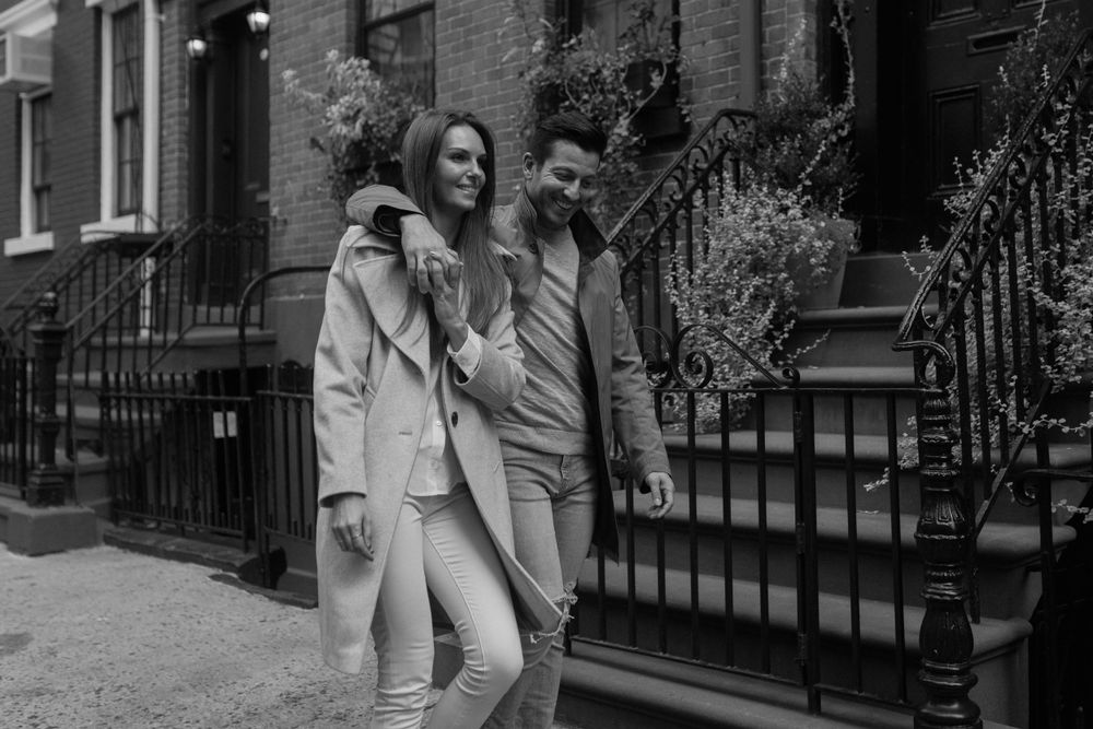 A couple laughing together while standing by iron railings outside a brownstone building.