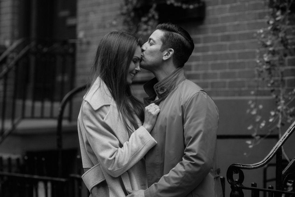 A romantic black and white portrait of a couple sharing an intimate kiss against a brick building.