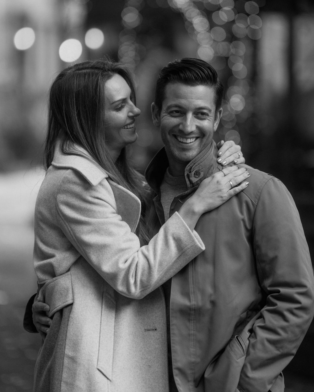 Black and white portrait of a couple sharing a joyful moment outdoors.
