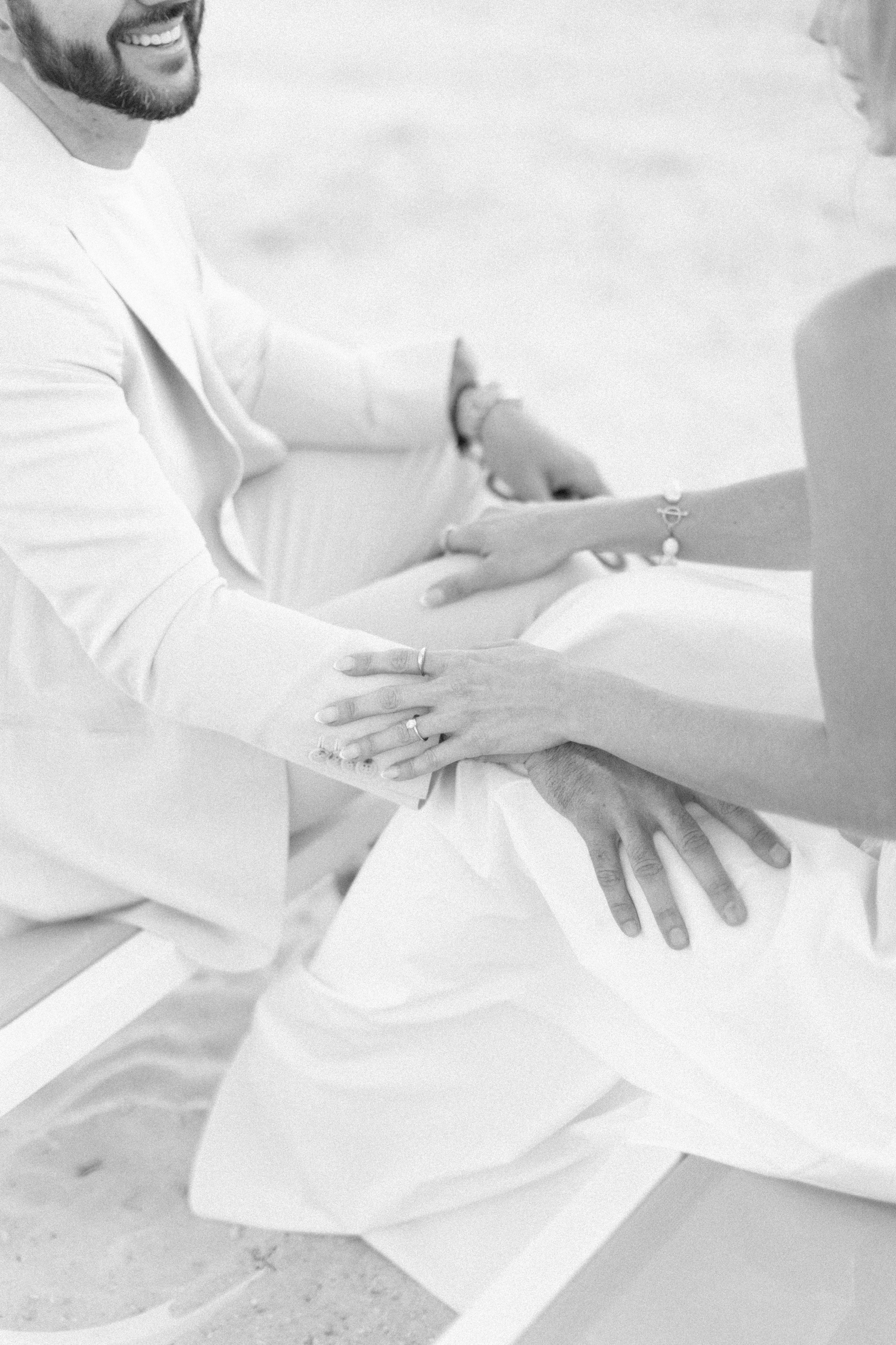 Close-up black and white photo showing hands touching in an intimate romantic moment, both wearing white clothing.