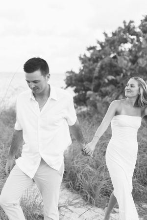 A joyful moment captured in black and white of a couple walking on a beach path.