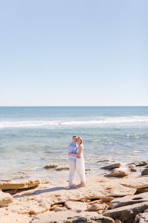 A romantic coastal scene with waves crashing against rocky shoreline under blue skies.