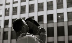 Two people share an intimate moment in front of an office building in black and white photography.