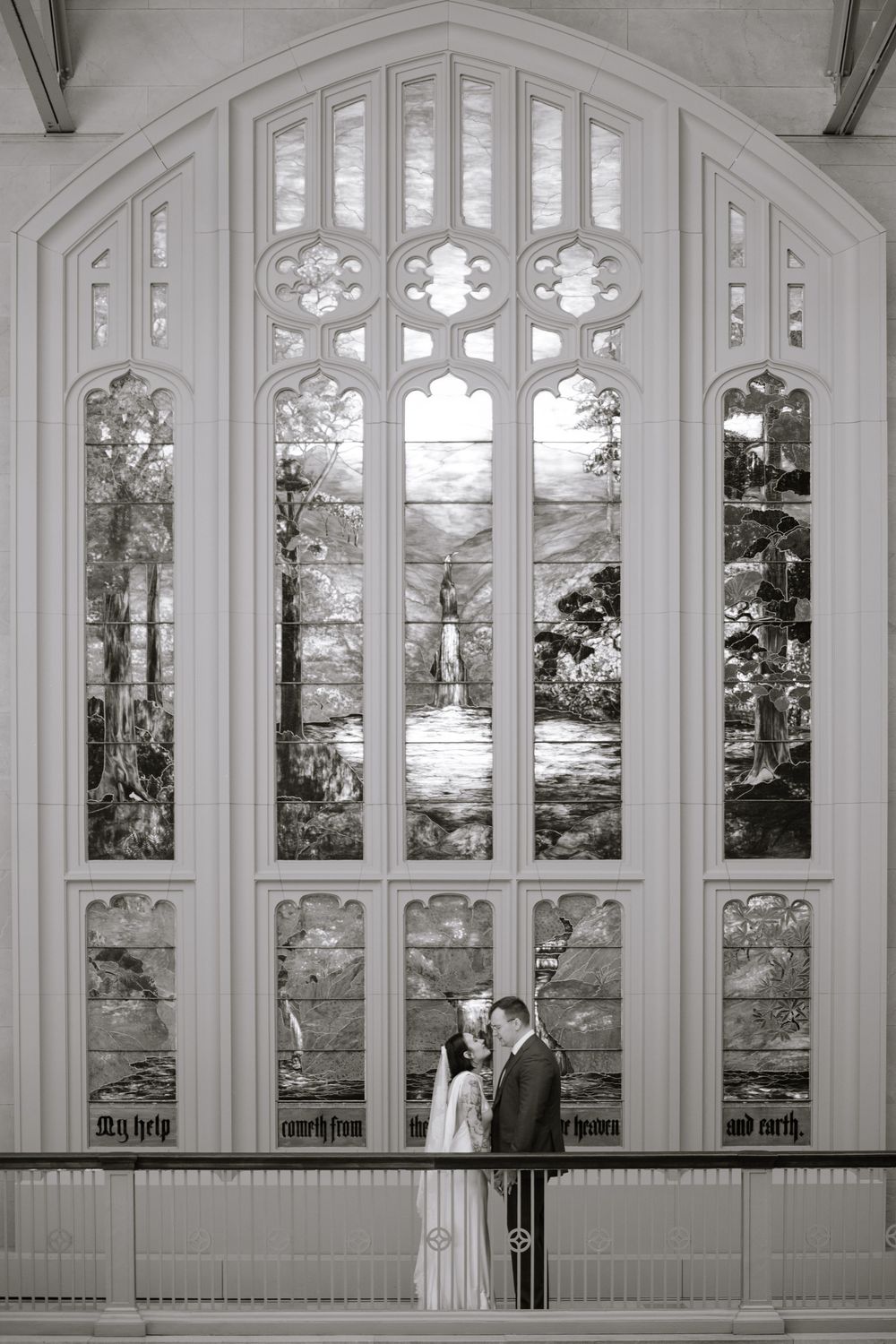 Bride and groom share a romantic moment before a stunning stained glass window in a historic church.