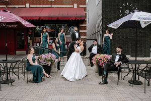 Wedding party poses on urban patio, bride and groom kissing while bridesmaids in teal gowns and groomsmen relax nearby.