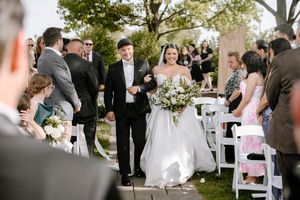 Bride and groom walking down outdoor aisle after ceremony, surrounded by smiling guests on a sunny day.