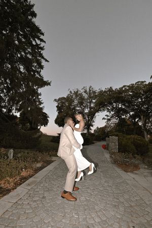 A couple shares a romantic moment on a cobblestone path at dusk with trees in the background.