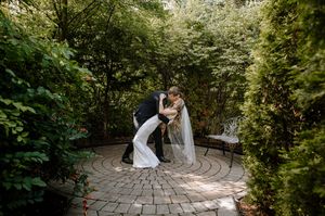 A couple shares an intimate moment on a circular stone patio surrounded by lush garden greenery in a romantic setting.