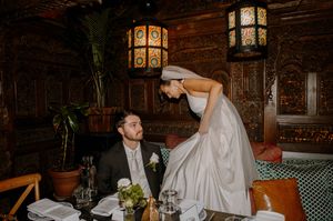 A couple shares a playful moment during their wedding reception at a rustic restaurant with vintage lanterns glowing.