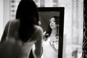 Black and white photo of a bride examining her reflection in a tall mirror while getting ready.