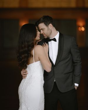 Elegant bride in white sequin gown and groom in dark tuxedo sharing a romantic moment at their wedding reception.