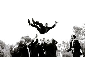 Groomsmen tossing groom into the air in a black and white outdoor wedding celebration photo.