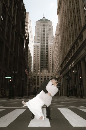 Groom dipping bride in a romantic kiss on a crosswalk with Chicago skyscrapers in background.