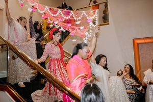 Women in vibrant Indian attire dance on a decorated staircase during a traditional wedding celebration.