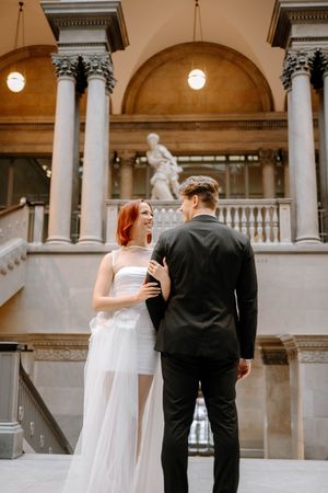 A couple shares a joyful moment in an elegant historic building with grand columns and marble architecture.