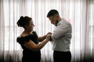 A couple dances together in front of sheer white curtains in a romantic ballroom setting.