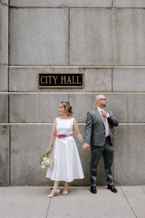 Artistic triptych of a bride and groom leaning against City Hall wall in stylish wedding attire.