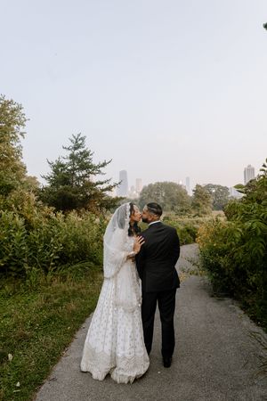 A bride and groom embrace on a garden path surrounded by lush greenery on their wedding day.