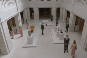 Elegant wedding reception in a classical white museum gallery with sculptures and guests in formal attire.