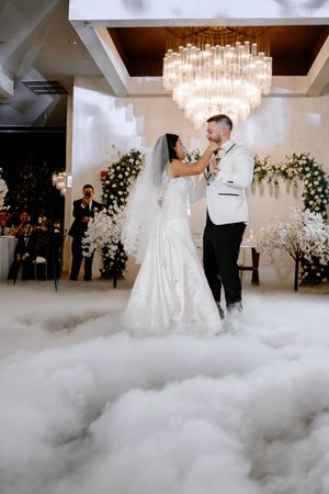 A couple shares their first dance at an elegant wedding reception with fog effects, chandelier and floral decorations.