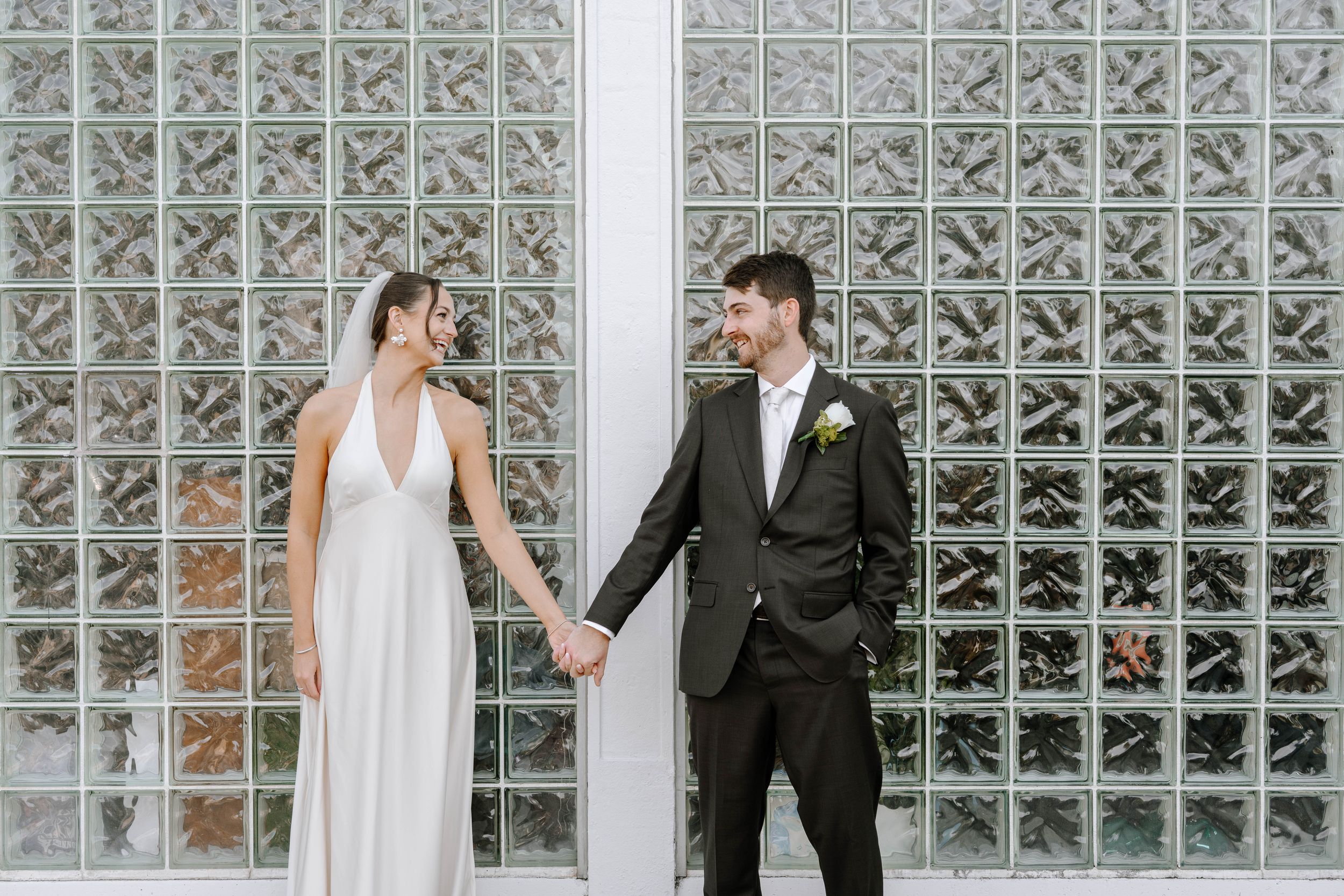 Newlywed couple poses in front of a modern glass block wall in a bright indoor setting.