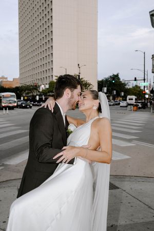 A romantic moment between newlyweds dancing on an urban sidewalk with tall buildings in the background.