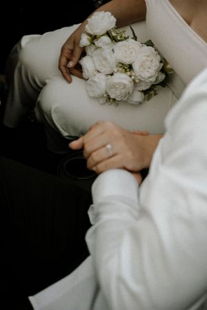 A white bridal bouquet of roses rests in someone's lap wearing winter white attire. Dream wedding photography Chicago.