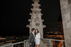 A couple poses romantically on a gothic church balcony at night with city lights glowing.  Best wedding photographers Chicago.