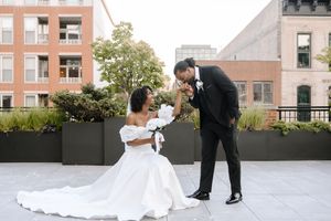 A newlywed couple shares a romantic moment on a modern rooftop terrace with city buildings in the background.