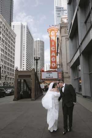 Bride and groom kissing in front of the iconic Chicago Theatre marquee on State Street with city skyscrapers in the background.