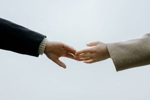 Two hands reaching towards each other against a white background in a minimalist composition.