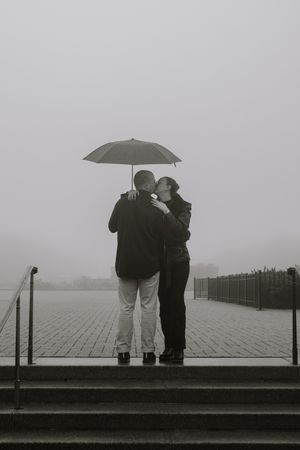 A series of black and white photos showing two people standing together in fog with an umbrella on stone steps.