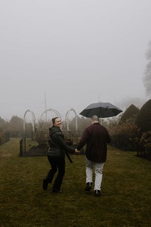 A group of people walk through a misty field with umbrellas on a foggy autumn day.