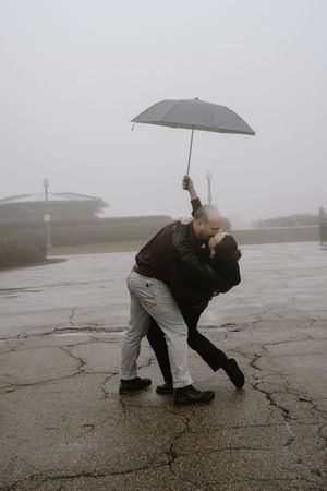 Two people with an umbrella lean into strong wind on a foggy day, demonstrating the power of stormy weather.