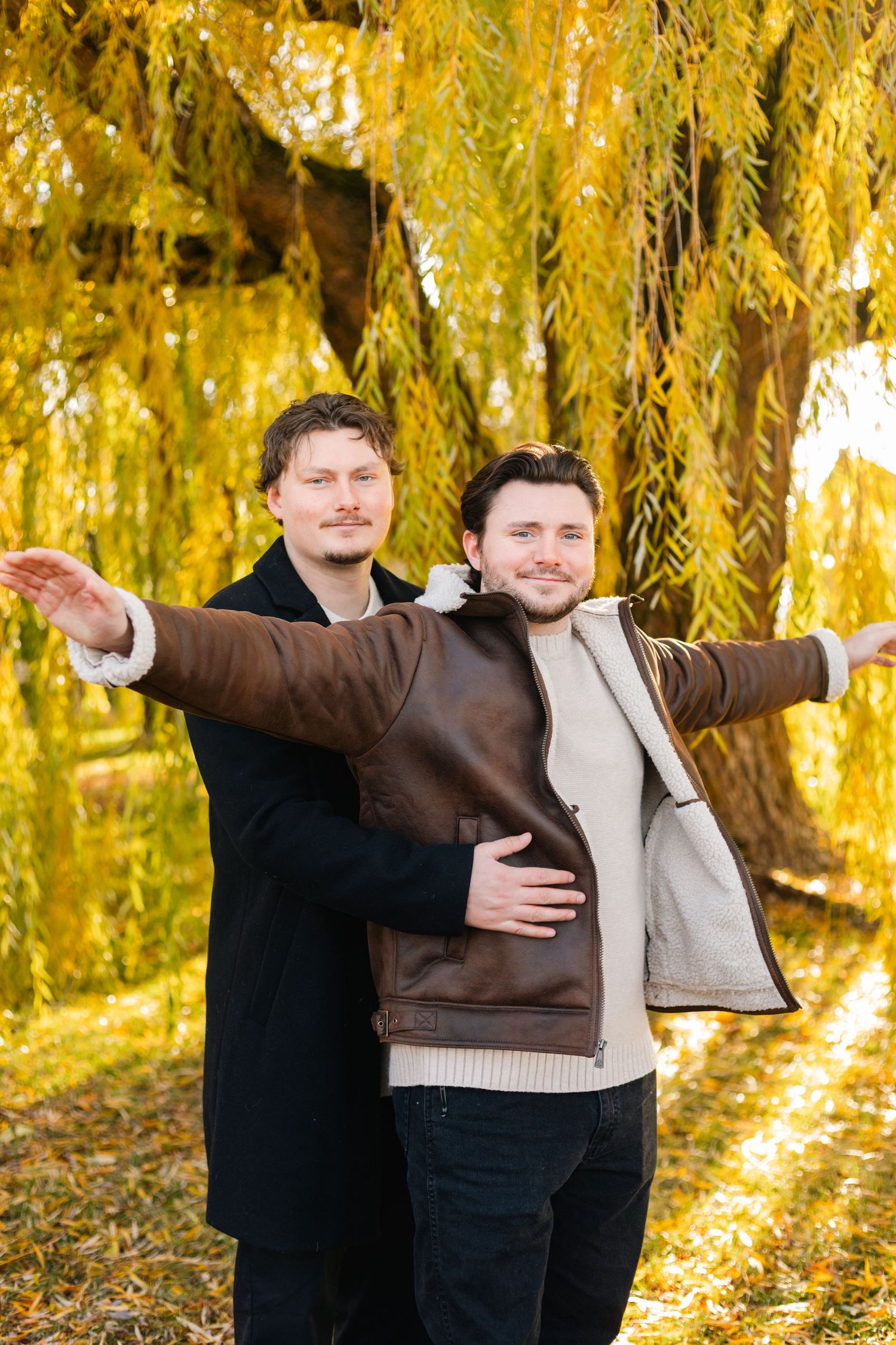 Group of people gathered under golden willow trees on autumn day.