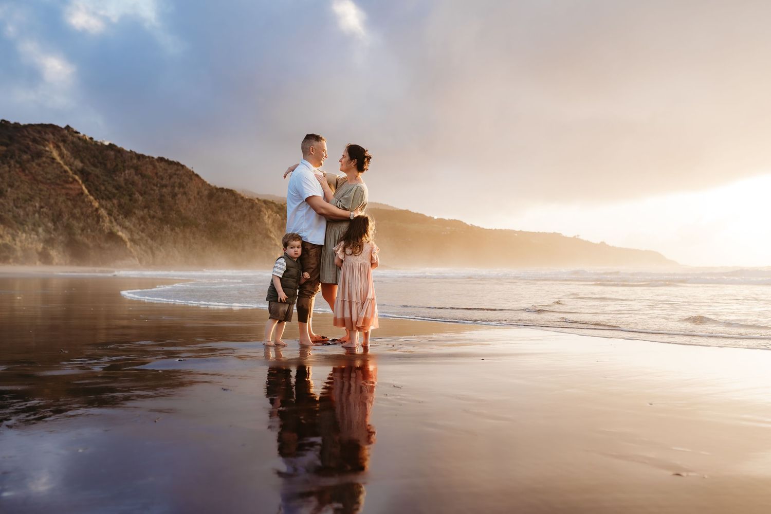 Couple embracing on misty beach at sunset with cliffs in background.