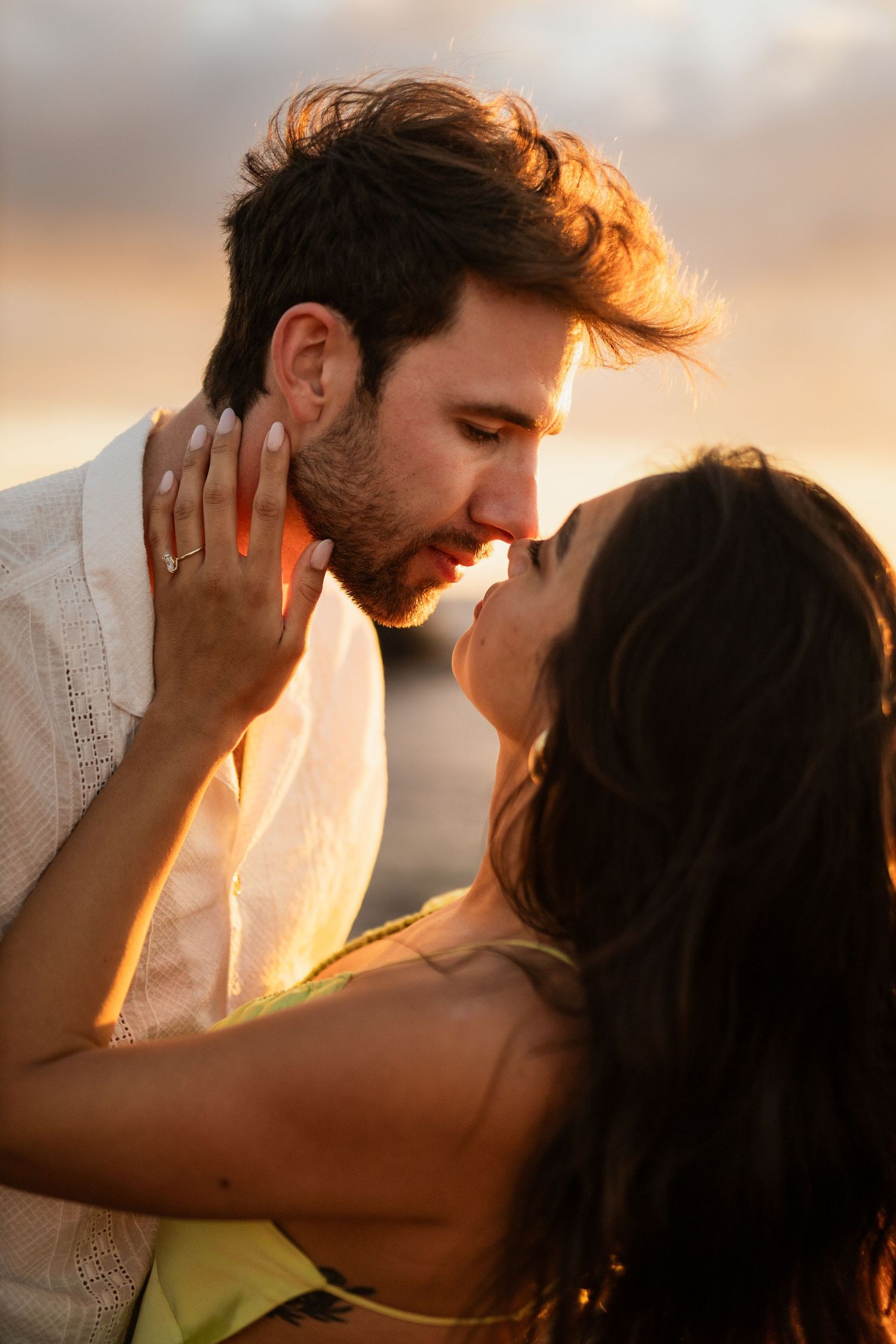 Couple sharing a romantic almost-kiss bathed in warm golden sunset light.