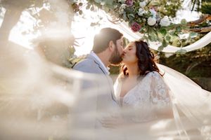 A romantic wedding moment captured with sunlight streaming through floral arrangements and flowing veil.