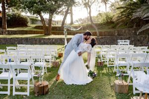 A romantic dip pose among white garden chairs at an outdoor wedding ceremony.