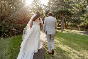 A wedding couple walking hand in hand down a sunlit garden path.