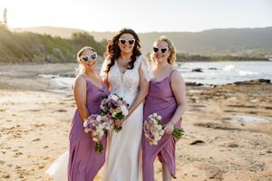 Wedding party in purple and white poses together on coastal beach.