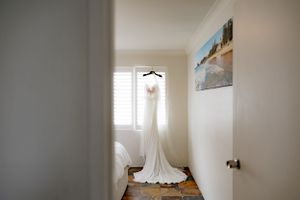 An elegant white wedding dress hanging in a sunlit hallway.